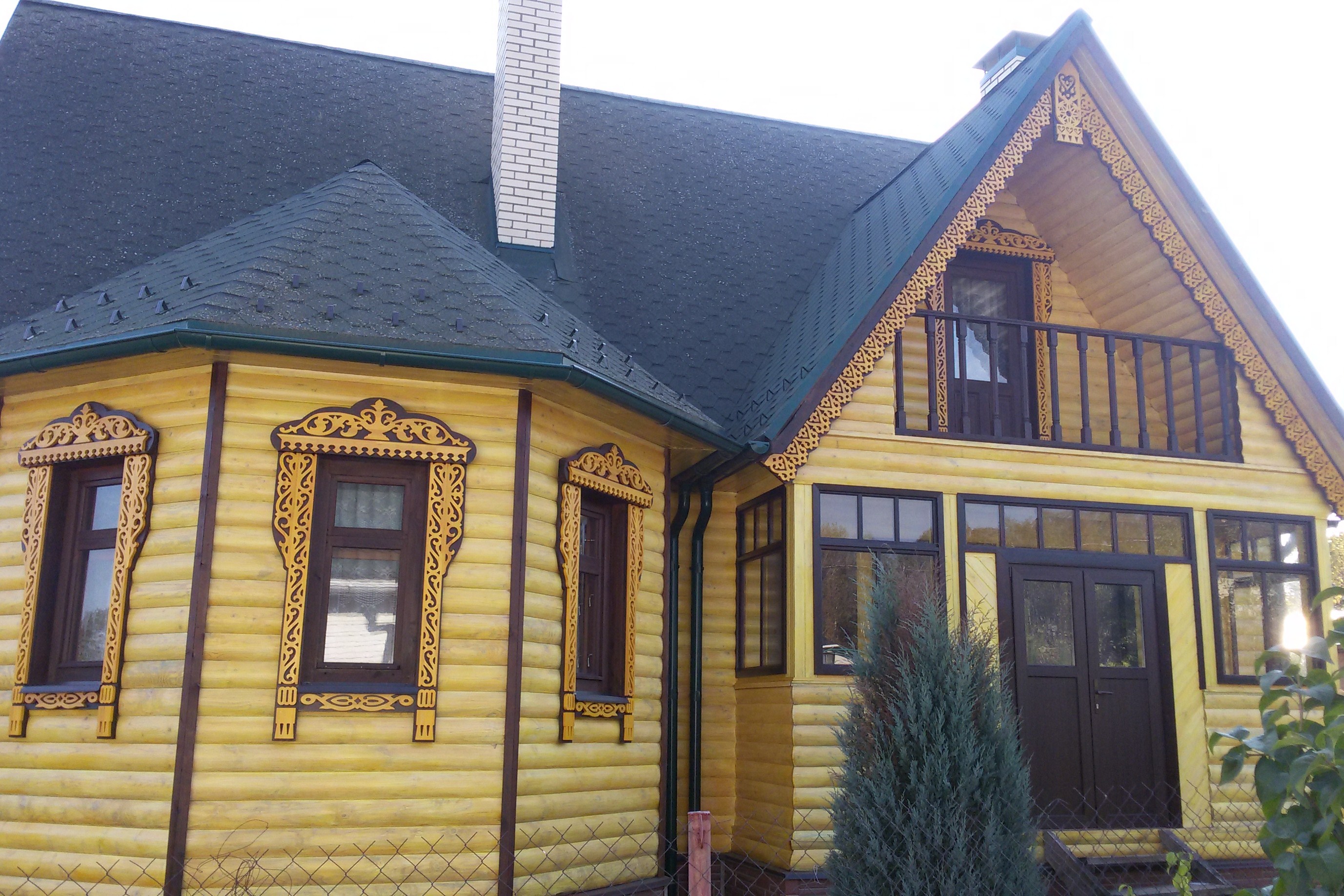 Фасад деревянного дома украшенный резными наличниками и карнизами